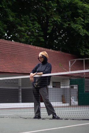 An Asian female model exudes confidence as she stands on a tennis court, dressed in jeans and a...