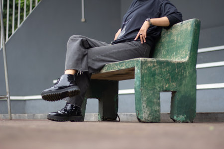 An Asian female model exudes a relaxed style, donning jeans and a black shirt while seated on a...