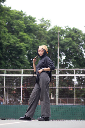 An Asian female model exudes confidence as she stands on a tennis court, dressed in jeans and a...