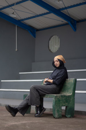 An Asian female model exudes a relaxed style, donning jeans and a black shirt while seated on a...