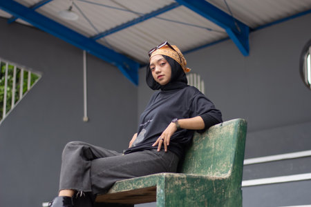 An Asian female model exudes a relaxed style, donning jeans and a black shirt while seated on a...