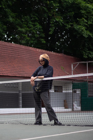 An Asian female model exudes confidence as she stands on a tennis court, dressed in jeans and a...