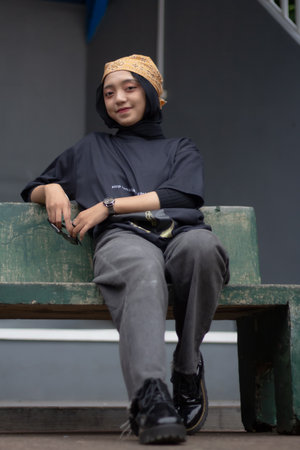 An Asian female model exudes a relaxed style, donning jeans and a black shirt while seated on a...