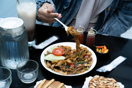 A photo of a hand enjoying a meal with a menu of Kwetiaw noodles, ice cream, water, and a milkshake...