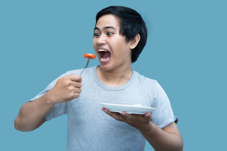 A man in a gray shirt is holding a fork and a plate containing food, for design and visual editing...
