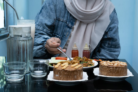 A photo of a hand enjoying a meal with a menu of Kwetiaw noodles, ice cream, water, and a milkshake on the tableの写真素材
