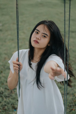 A childhood dream of flying high on a swing in a park. A young girl in a white dress rides on a swingの写真素材