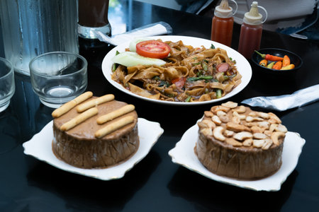 A photo of a hand enjoying a meal with a menu of Kwetiaw noodles, ice cream, water, and a milkshake...