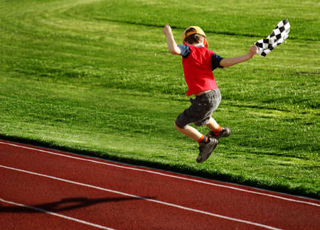 Boy with a checked flag jumping on a racetrackの写真素材