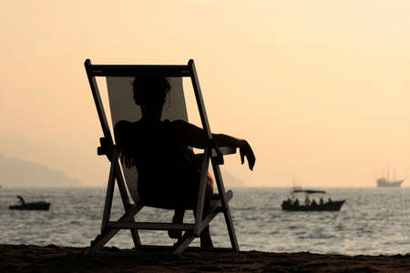 Woman sitting in the chair watching sunset at the beachの写真素材