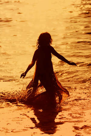 Woman running in the water at sunsetの写真素材