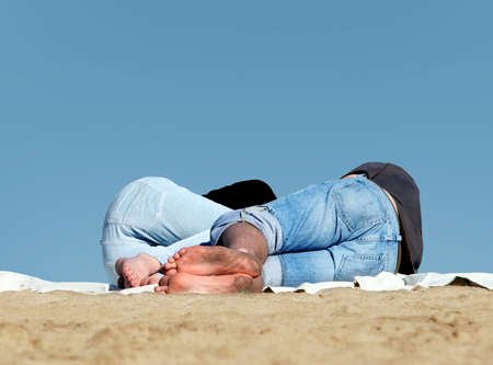 Couple sleeping on the beach with blue sky as a backgroundの写真素材
