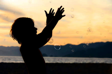 Boy playing with bubbles on the beach at sunsetの写真素材