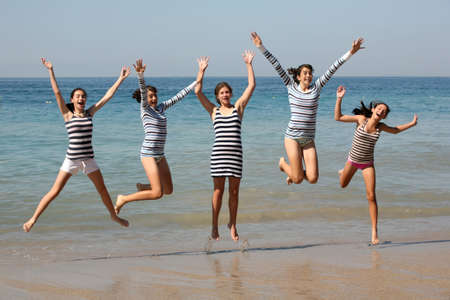 Five teenage girls jumping on the beachの写真素材
