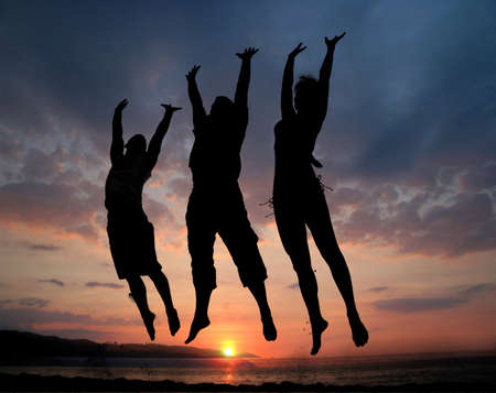Three people silhouettes jumping on the beachの写真素材