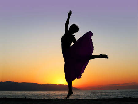 Dramatic image of a woman dancing by the ocean at sunsetの写真素材