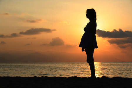 Pregnant woman standing on the beach at sunsetの写真素材