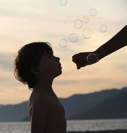 Boy playing with bubbles on the beach at sunsetの写真素材