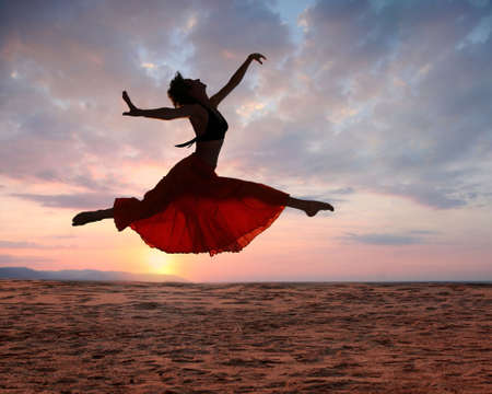 Dramatic image of a woman jumping above the ocean at sunset, silhouetteの写真素材