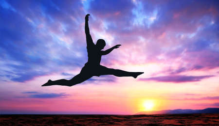 A silhouette of a jumping man on a colorful sunset backgroundの写真素材