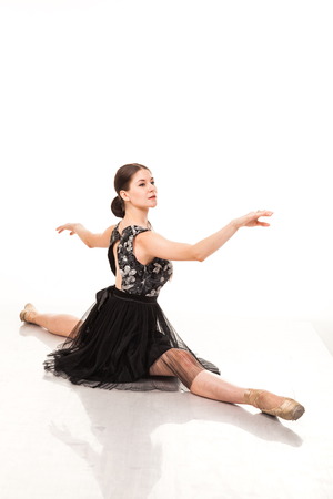 Beautiful young ballerina, isolated on white background. In pointes and black ballet tutu. Sits on the twine, shows different poses. graceful brunette with long hairの写真素材