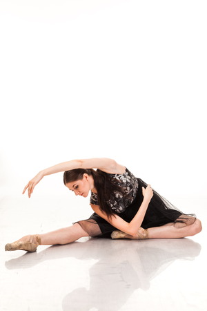 Beautiful young ballerina, isolated on white background. In pointes and black ballet tutu. Sits on the twine, shows different poses. graceful brunette with long hairの写真素材