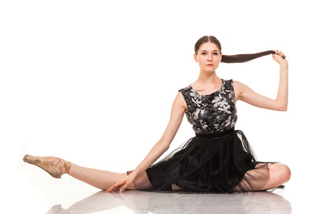 Beautiful young ballerina, isolated on white background. In pointes and black ballet tutu. Sits on the twine, shows different poses. graceful brunette with long hairの写真素材