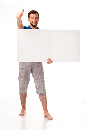 A guy with a beard posing with a white sign. Shows different emotions. Isolated on a white background. In a gray trousers and a blue T-shirt. For advertising, logo, business cards, contact phones, etcの写真素材