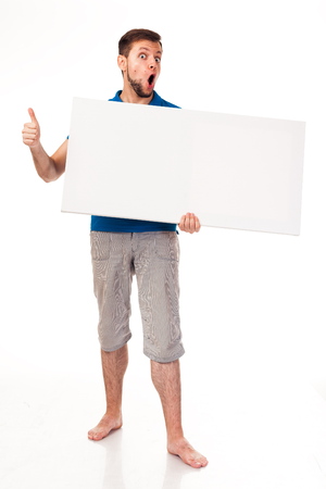A guy with a beard posing with a white sign. Shows different emotions. Isolated on a white background. In a gray trousers and a blue T-shirt. For advertising, logo, business cards, contact phones, etcの写真素材