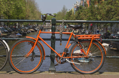 Dutch orange bike on canal bridge in Amsterdam with canal boat on backgroundの写真素材