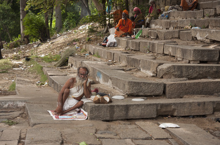 White dressed hinduist Sadhu monk resting on stone steps of Cauveri riverのeditorial素材