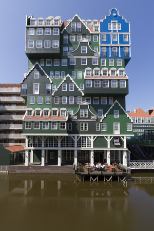 Zaandam, the Netherlands Eccentric modern architecture of hotel in city center of Zaandam, consisting of stacked facades of typical Dutch wooden green gable houses, with hotel guests having lunch on terrace above water on a bright summer dayのeditorial素材