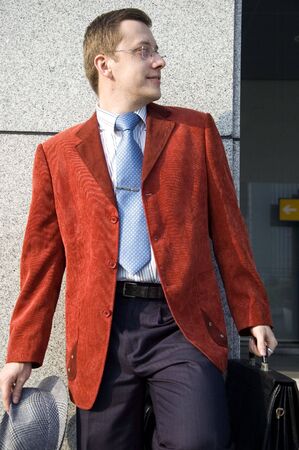 Young, successful European businessman in modern Chinese city. Wearing red suit, holding briefcase and hat.の写真素材