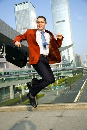 Happy, successful businessman - jumping. Wearing red suit and blue tie. Modern skyscrapers as background.の写真素材