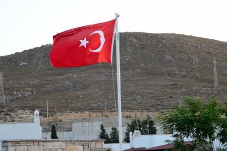 Turkish flag in Bagla, holiday resort near Bodrum. Behind hills and buildings.の写真素材