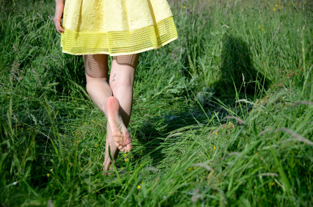 Female walks on the grass with barefoot. Young woman enjoys outdoor walk, nature, green fields and blue sky.の写真素材