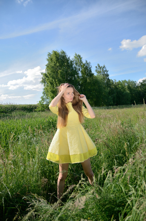 Petite woman, wearing yellow dress, posing in the meadow with high grass, tress as background. Female model and nature.の写真素材
