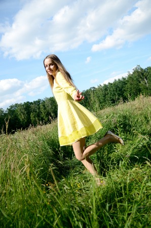 Petite woman, wearing yellow dress, dancing in the meadow. Female model and nature.の写真素材