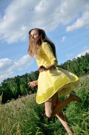 Petite woman, wearing yellow dress, dancing in the meadow. Female model and nature.の写真素材