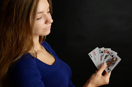 Young woman portrait with black background. Female model holding five poker cards.