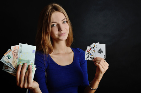 Young woman portrait with black background. Female model holding five poker cards and money, dollars and euro banknotes.の写真素材