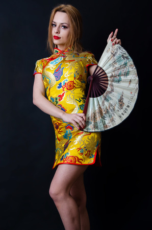 Shapely girl from Poland. Young female model posing in studio with black background. Caucasian girl with colorful Chinese dress and fan.の写真素材