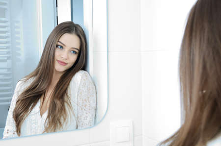 Young woman in bathroom. Polish model smiling in the mirror reflection.
