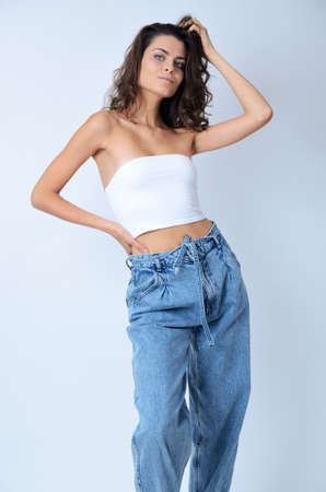 Young Polish woman in studio. Slim woman with dark hairs wearing white top and blue jeans.の写真素材
