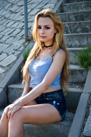 Beautiful, young woman posing for outdoor photos. Summer in Poland.Woman sitting on stairs with blue top and shorts.の写真素材