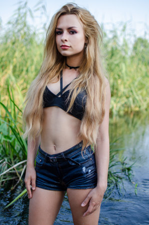 Beautiful, young woman posing for outdoor photos. Attractive woman in river, wearing black top and jeans shorts. Summer in Poland.の写真素材