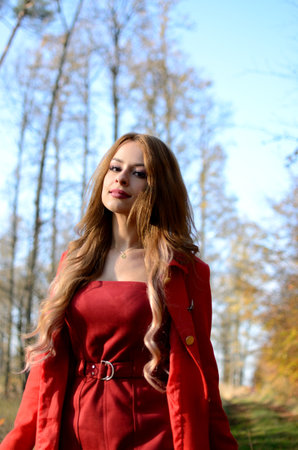 Warm autumn in Poland. Young woman with red dress surrounded by trees. Woman with blonde hair extension.の写真素材