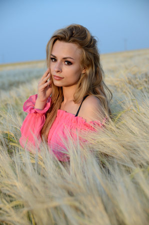 Charming, young woman posing in field of rye. Woman wearing pinky top.の写真素材