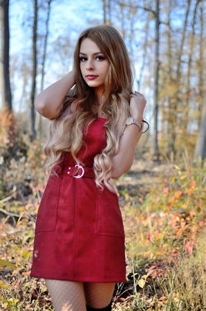 Warm autumn in Poland. Young woman with red dress surrounded by trees. Woman with blonde hair extension.の写真素材
