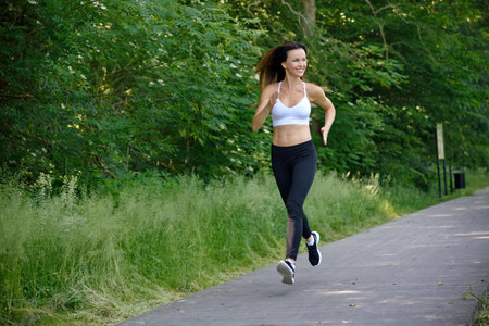 Fit woman in her 30's jogging in the park. Young woman with black trousers and white top in the park.の写真素材